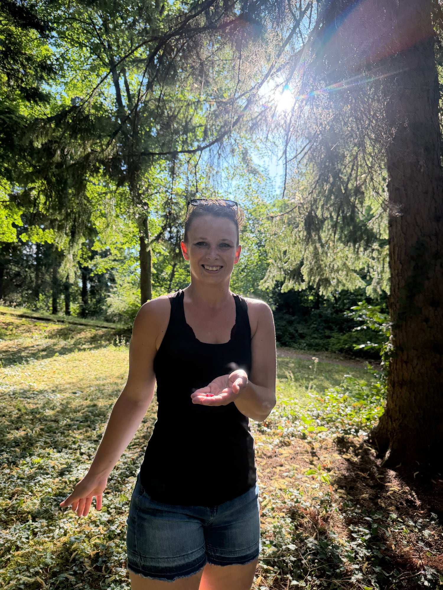 Anja von Kopflichtung steht lächelnd im Wald und streckt die Hand aus
