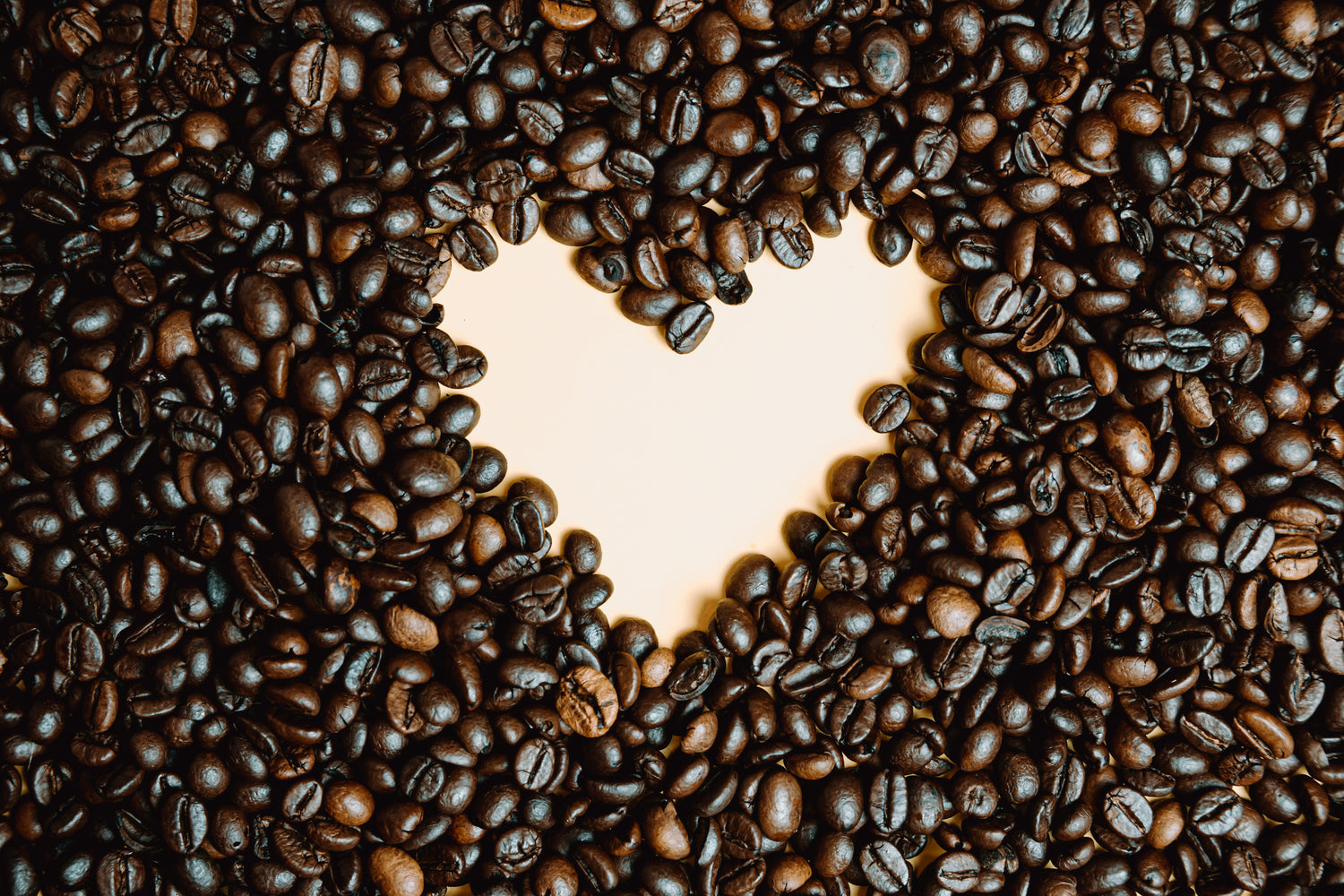 ausgestreute geröstete Kaffeebohnen auf hellem Untergrund, welche in der Mitte ein Herz zeigen